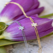 Two star-shaped necklace pendants on chains with purple tulips in the background.