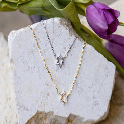 Gold necklace with star pendant on a stone surface with purple tulips in the background